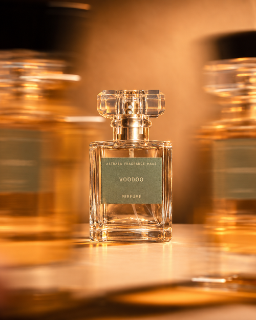 Voodoo perfume bottle by Astraea Fragrance Haus with a clear glass rectangular shape and decorative cap, blurred background with warm lighting.