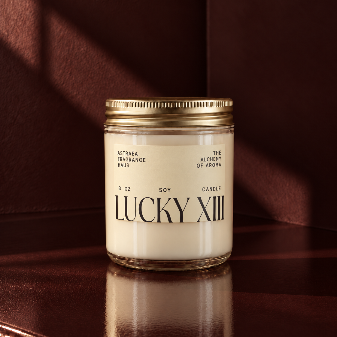 Asterae Fragrance Haus Lucky XIII soy candle in a clear glass jar with a gold lid, placed on a dark wooden surface against a maroon background.