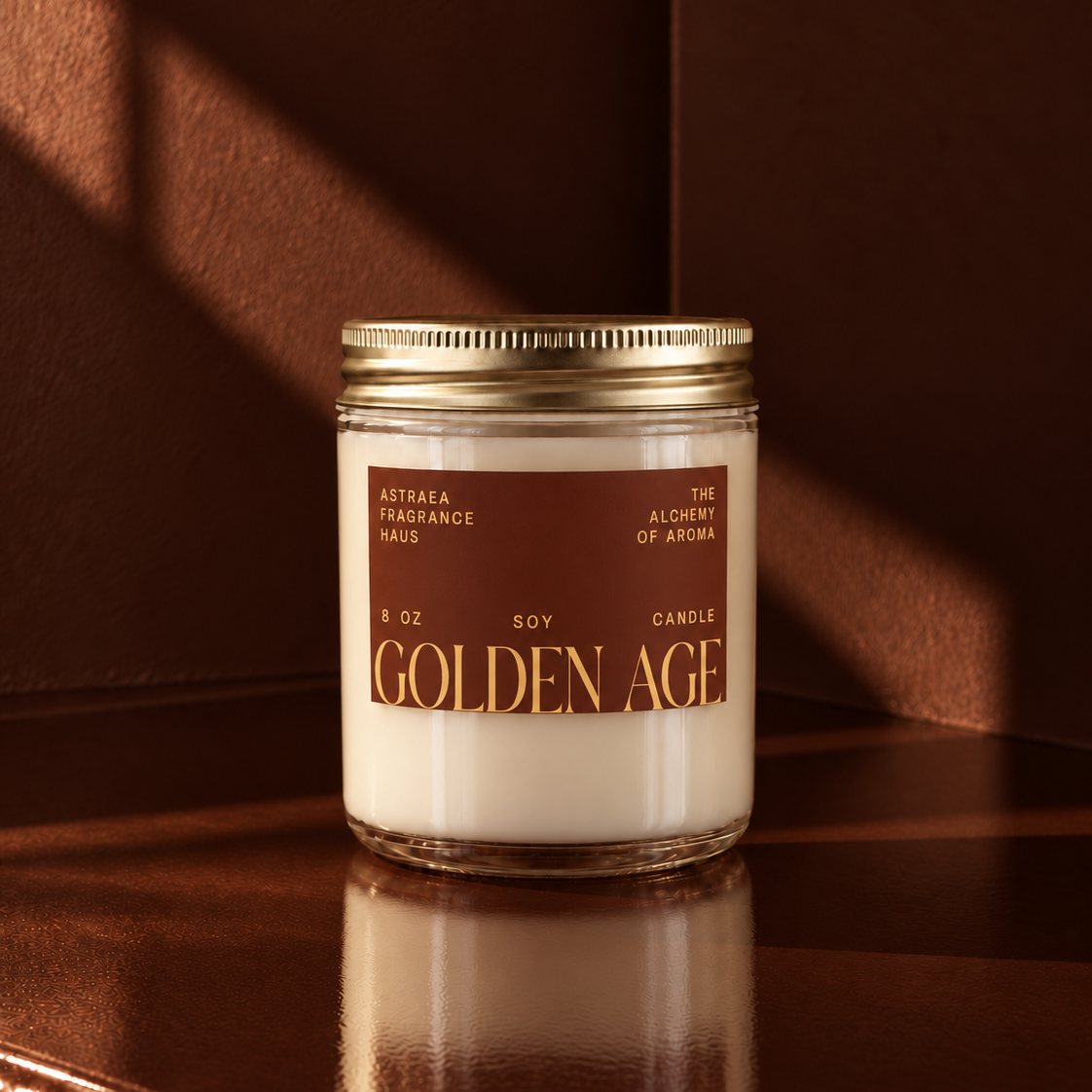 Golden Age soy candle by Astraea Fragrance Haus in a clear glass jar with a gold lid, featuring a brown and gold label, placed on a wooden surface.